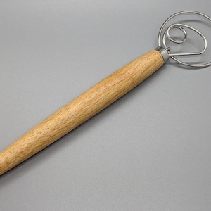 May include: A wooden handled dough whisk with a circular wire frame. The whisk is made of stainless steel and has a long wooden handle.