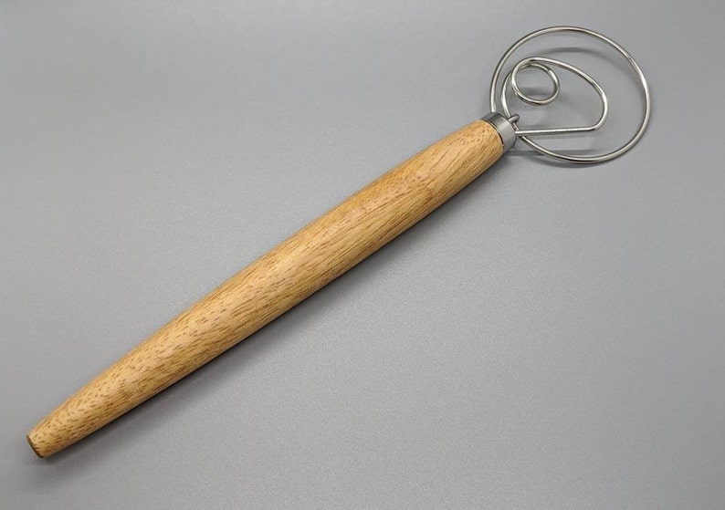 May include: A wooden handled dough whisk with a circular wire frame. The whisk is made of stainless steel and has a long wooden handle.