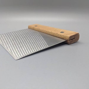 Puede incluir: Una esp&aacute;tula para reposter&iacute;a de acero inoxidable con mango de madera. El mango tiene dos puntos negros en la parte superior.