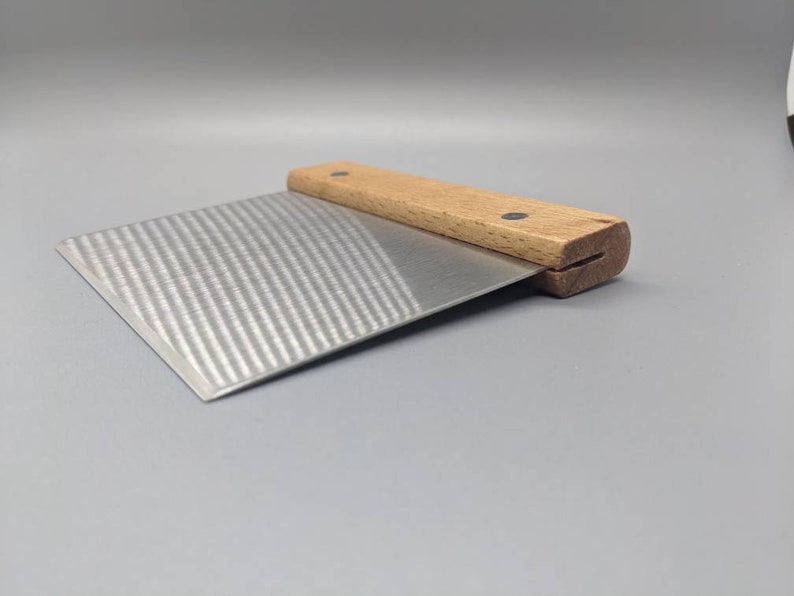 Puede incluir: Una esp&aacute;tula para reposter&iacute;a de acero inoxidable con mango de madera. El mango tiene dos puntos negros en la parte superior.