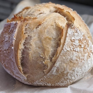 Puede incluir: Una hogaza de pan de masa madre reci&eacute;n horneada con una corteza ligeramente crujiente y un interior suave y aireado.