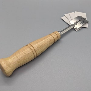 Puede incluir: Una herramienta con mango de madera y una cuchilla de acero inoxidable para raspar. La cuchilla est&aacute; etiquetada como "Stainless Blade".