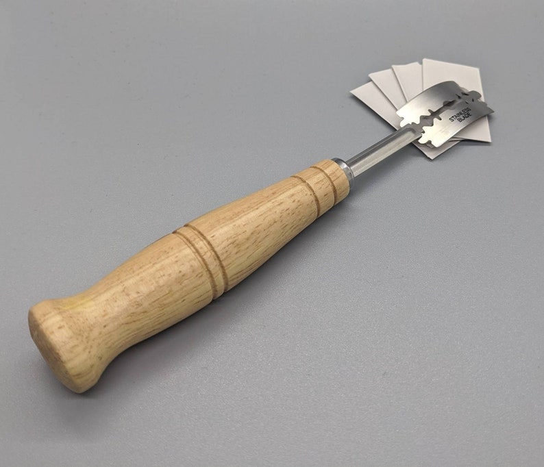 Puede incluir: Una herramienta con mango de madera y una cuchilla de acero inoxidable para raspar. La cuchilla est&aacute; etiquetada como "Stainless Blade".