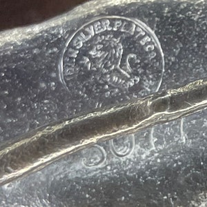 May include: Close-up of a silver-plated item with a lion logo and the words "Silver Plated" inscribed on the surface.