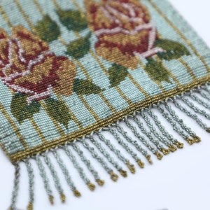 Peut inclure: Un sac &agrave; main vintage en perles avec un fond ray&eacute; bleu et or et un motif floral compos&eacute; de deux roses rouges et jaunes. Le sac &agrave; main a une frange argent&eacute;e.