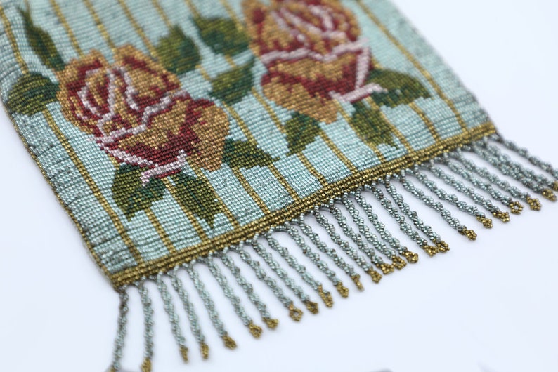 Peut inclure: Un sac &agrave; main vintage en perles avec un fond ray&eacute; bleu et or et un motif floral compos&eacute; de deux roses rouges et jaunes. Le sac &agrave; main a une frange argent&eacute;e.