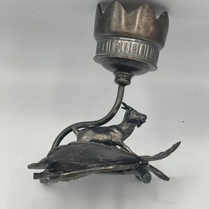 May include: Silver candlestick with a goat on a turtle base. The candlestick has a crown-shaped top.