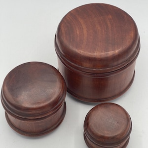 May include: Three wooden boxes of varying sizes. The boxes are all round and have a dark brown finish. The largest box is in the background, and the smallest box is in the foreground.