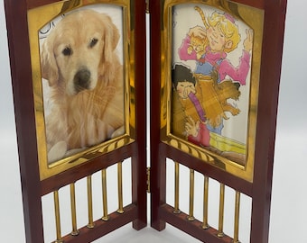 May include: A two-panel wooden picture frame with a brass trim. The left panel features a photo of a golden retriever dog. The right panel features a photo of a girl holding a kitten with a dog in the background. The frame has a brass lattice design on the bottom.