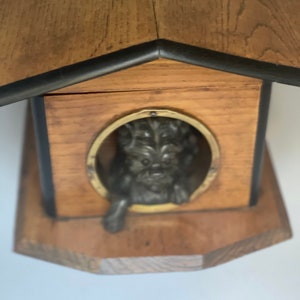 Könnte beinhalten: Ein hölzernes Hundehaus mit schwarzem Rand und einer Metall-Hundefigur, die aus dem Türloch schaut.