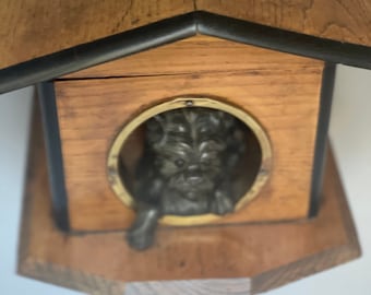 May include: A wooden dog house with a black trim and a metal dog figurine peeking out of the door hole.
