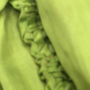 Peut inclure: Gros plan sur un tissu vert &agrave; texture pliss&eacute;e. Le tissu est pli&eacute; et drap&eacute;, cr&eacute;ant un aspect doux et fluide.