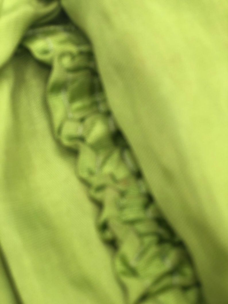 Peut inclure: Gros plan sur un tissu vert &agrave; texture pliss&eacute;e. Le tissu est pli&eacute; et drap&eacute;, cr&eacute;ant un aspect doux et fluide.