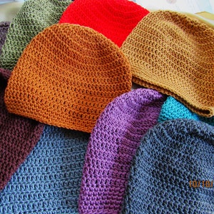 May include: A collection of handmade crochet beanies in various colors, including orange, red, teal, purple, and brown. The beanies are displayed in a close-up shot, showcasing the textured stitch pattern and the range of hues. The date 10/10/2023 is visible.