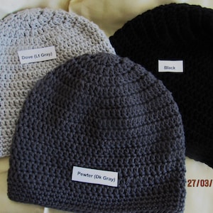 May include: Three crocheted beanies in dove gray, pewter gray, and black. Each beanie has a label indicating its color. The dove gray beanie is labeled "Dove (Lt Gray)", the pewter gray beanie is labeled "Pewter (Dk Gray)", and the black beanie is labeled "Black".