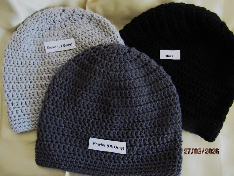 May include: Three crocheted beanies in dove gray, pewter gray, and black. Each beanie has a label indicating its color. The dove gray beanie is labeled "Dove (Lt Gray)", the pewter gray beanie is labeled "Pewter (Dk Gray)", and the black beanie is labeled "Black".