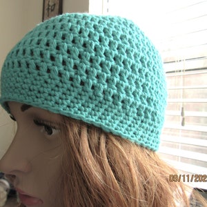 May include: A turquoise crochet beanie hat. The hat is made with a textured stitch pattern, creating a breathable design. The hat is a solid color and appears to be handmade. The beanie is a close-fitting style, suitable for casual wear.
