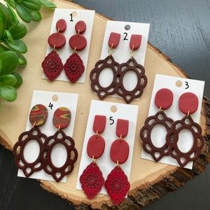 Könnte beinhalten: Fünf Paar handgefertigte Ohrringe aus Polymer Clay in verschiedenen Stilen. Die Ohrringe werden auf weißen Karten mit den Nummern 1 bis 5 präsentiert. Die Ohrringe haben rote, braune und marmorierte Designs.