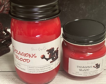Può includere: Due candele di soia rosse in barattoli di vetro con coperchi neri. Le etichette riportano "Dragons Blood" e elencano le fragranze: ambra, incenso, patchouli, rosa, gelsomino, lillà, arancia rossa, pompelmo e vaniglia del Madagascar.