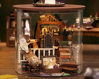 May include: A miniature glass jar with a wooden lid, containing a miniature scene of a wizard's study. The scene includes a wooden desk, a bookshelf, a white owl, a crystal ball, and a black candlestick with lit candles. The lid of the jar features a miniature witch's hat with a black pointed top and a brown brim.