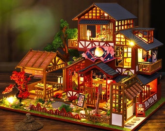 May include: A miniature wooden dollhouse with a Japanese theme. The dollhouse is multi-level and features a red and brown exterior with a black roof. The dollhouse is lit with small lights and has a small garden with a pond and a fence.