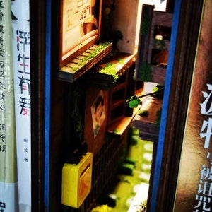 以下が含まれることがあります： 黄色の郵便受け、緑の植物、黒い文字で「江牛、夜呪いの子供」と書かれた木製の看板のある、日本の路地のミニチュアモデルです。