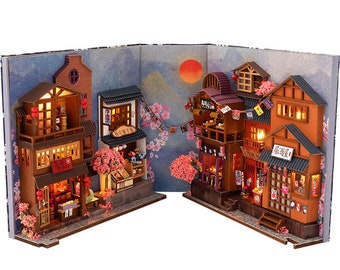 Pode incluir: Um modelo de casa de bonecas em miniatura de uma cena de rua japonesa com vários edifícios, lanternas vermelhas e árvores de cerejeira em flor. Os edifícios têm fachadas detalhadas com janelas, portas e placas em caracteres japoneses.