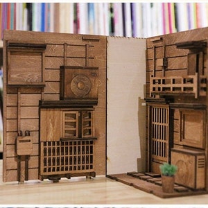 以下が含まれることがあります： レーザーカットされた木材で作られた、複数の建物と小さな鉢植えの植物がある日本の街並みの木製模型。組み立てて楽しむことができます。