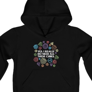 Op de afbeelding: Zwart hoodie met een kleurrijke afbeelding van dobbelstenen en de tekst "Ja, ik heb echt al deze dobbelstenen nodig."