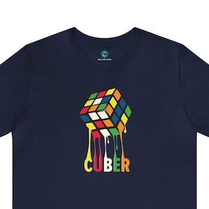 Op de afbeelding: Een marineblauw t-shirt met een kleurrijke, smeltende Rubik's Cube-afbeelding en de tekst "CUBER" gedrukt op de voorkant.