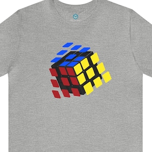 Op de afbeelding: Een heidegrijs T-shirt met een kleurrijke Rubik's Cube-afbeelding. De kubus is in 3D-perspectief en lijkt uit elkaar te vallen.
