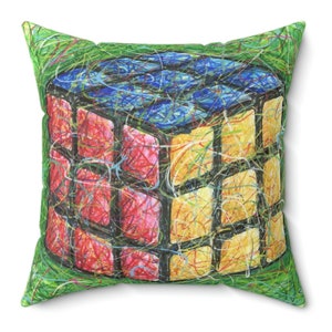 May include: A green pillow with a colorful Rubik's Cube design. The cube is drawn in a scribbled style with red, yellow, blue, and black colors.
