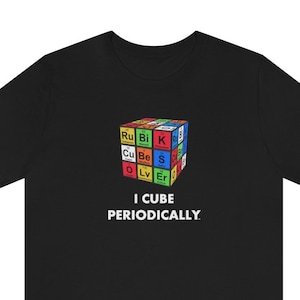 Op de afbeelding: Zwart T-shirt met een witte afbeelding van een Rubik's Cube gemaakt van chemische element symbolen. De tekst "I cube periodically." staat onder de afbeelding.