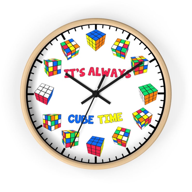 Op de afbeelding: Een witte ronde klok met een houten frame. De wijzerplaat van de klok is zwart-wit met zwarte wijzers. De wijzerplaat van de klok is versierd met kleurrijke Rubik's Cubes rond de wijzerplaat. De tekst "It's Always Cube Time" is gedrukt op de wijzerplaat van de klok.