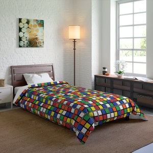 May include: A twin-sized bed with a colorful duvet cover featuring a repeating pattern of squares in red, blue, green, yellow, and white, resembling a Rubik's Cube. The bed is made with a white pillow and a white bed frame.