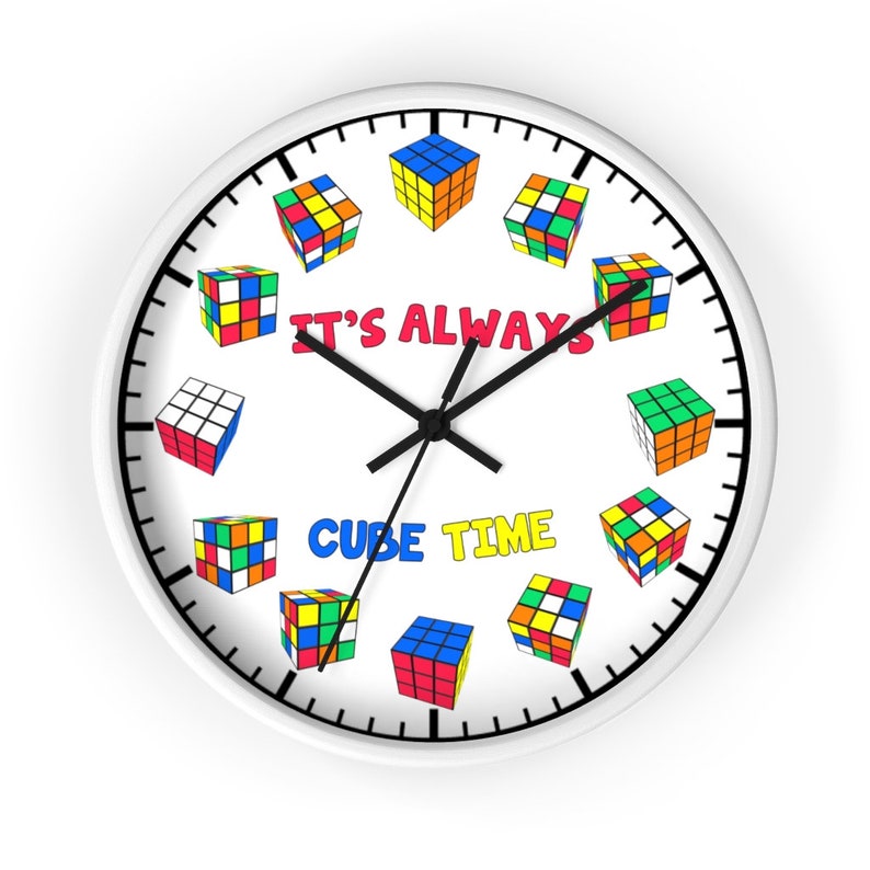 Op de afbeelding: Witte ronde klok met zwarte wijzers en een witte achtergrond. De wijzerplaat heeft een zwarte rand en zwarte markeringen voor de uren en minuten. De wijzerplaat heeft ook een kleurrijk Rubik's Cube-ontwerp met de tekst "It's Always Cube Time".