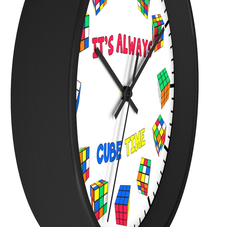 Op de afbeelding: Een zwart-witte klok met een witte wijzerplaat en zwarte wijzers. De wijzerplaat van de klok heeft een kleurrijk ontwerp van Rubik's Cubes en de tekst "It's Always Cube Time".