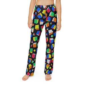 Op de afbeelding: Zwarte pyjamabroek met een kleurrijk Rubik's Cube-patroon. De kubussen zijn in verschillende maten en oriëntaties, met rode, blauwe, groene, gele, oranje en witte vierkanten. De broek heeft een rechte pijp.