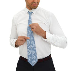 May include: A light blue tie featuring a repeating pattern of white geometric shapes, including cubes, pyramids, and other polyhedrons. The tie is being adjusted by a person wearing a white dress shirt.