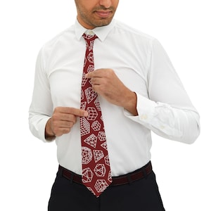 May include: A burgundy tie with a repeating geometric pattern of white cube and diamond shapes. The tie is being adjusted by a person wearing a white dress shirt and dark trousers. A classic accessory.