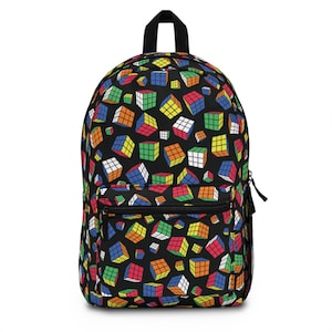 Op de afbeelding: Zwarte rugzak met een kleurrijk patroon van Rubik's Cubes. De rugzak heeft een voorvak met ritssluiting, een handvat aan de bovenkant en zwarte schouderbanden. De Rubik's Cubes zijn in verschillende formaten en posities.