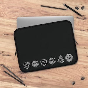 以下が含まれることがあります： 白の幾何学模様が施された黒いラップトップスリーブ。スリーブには、立方体、ピラミッド、球体など、3D形状の白い線画が描かれています。スリーブは長方形で、ジッパー開閉式です。