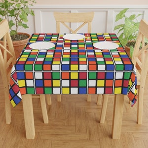 May include: A colorful tablecloth with a Rubik's Cube pattern. The tablecloth is laid on a wooden table with two chairs. The tablecloth is red, blue, green, yellow, white, and black.
