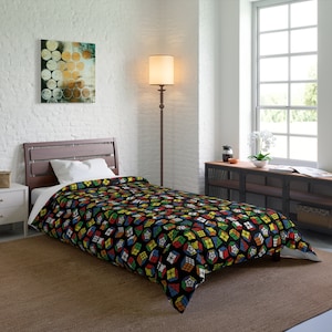 May include: A black twin-size duvet cover with a colorful Rubik's Cube pattern. The duvet cover is on a bed with a white pillow and a brown headboard. The bed is in a bedroom with a white brick wall, a floor lamp, and a window.