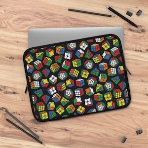 May include: Black laptop sleeve with a vibrant pattern of Rubik's Cubes and geometric puzzles. The sleeve has a black zip. The design features red, yellow, blue, green, and white cubes. The sleeve is designed to protect a laptop.