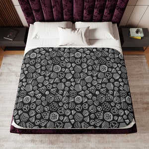 以下が含まれることがあります： 黒と白の幾何学模様の寝具。黒の背景に、白い輪郭の立方体、球体、ピラミッドが繰り返しデザインされています。