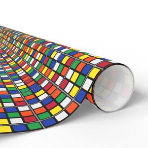 May include: Rolled-up wrapping paper featuring a colorful Rubik's Cube pattern. The design includes squares in red, blue, green, yellow, and orange, with white and black borders. The paper is partially unrolled, revealing the pattern.