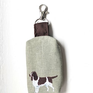 May include: A small, light green fabric pouch with a brown fabric top and a silver clip. The pouch has a brown and white dog silhouette printed on the front.