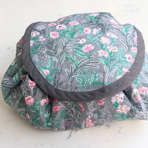 May include: A grey fabric pouch with a floral print featuring pink and green flowers. The pouch has a grey fabric trim around the top edge.