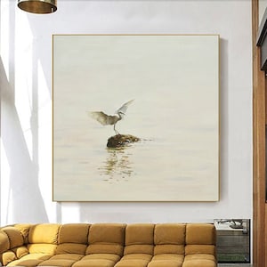 Puede incluir: Una pintura de acuarela de un p&aacute;jaro blanco con las alas extendidas de pie sobre una roca en un cuerpo de agua. El fondo es de color beige claro.